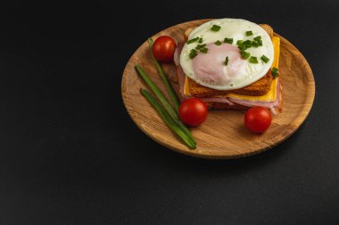 Tatmin edici bir kahvaltı sandviçi kızarmış ekmek, erimiş peynir ve mükemmel haşlanmış yumurta içerir. Beraberinde olgun kiraz domatesleri ve taze yeşil soğanlar, renkli bir yemek oluşturur..