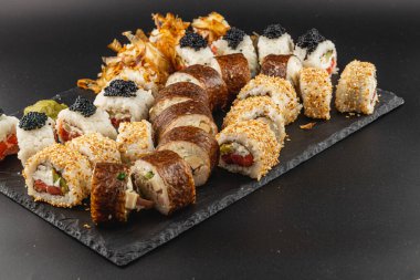 Özenle hazırlanmış bir suşi tabağında havyar ve susam da dahil olmak üzere çeşitli ekmekler sergileniyor. Koyu renkli tahta, suşinin parlak renkleriyle çelişiyor..