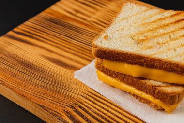 İki dilim altın-kahverengi ekmek arasında erimiş peynirli ızgara peynirli sandviç ahşap bir tahtanın üzerinde duruyor. Tatmin edici bir kahvaltı, brunch ya da atıştırmalık için ideal..