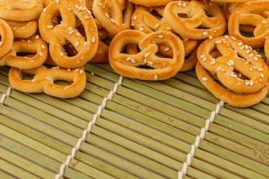 Delightful mini pretzels coated with sesame seeds rest on a bamboo mat, showcasing their golden brown color and crunch. Perfect for snacking at parties or casual gatherings. clipart