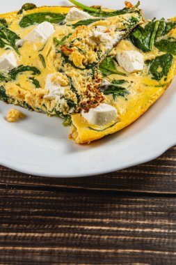 Lezzetli bir ıspanak ve feta omleti beyaz bir tabakta sunulur, yeşil ıspanak, parçalanmış feta ve altın yumurta karışımı sergilenir. Bu yemek sağlıklı bir kahvaltı için mükemmel..