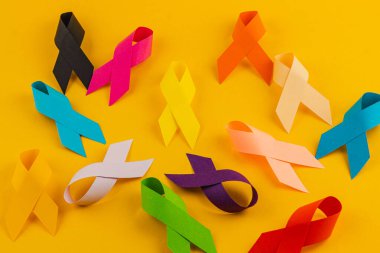 Çeşitli renklerde farkındalık kurdeleleri parlak sarı bir arka plana saçılmış, kanser, şeker hastalığı ve diğerleri gibi birden fazla sağlık sorununa verilen desteği sembolize ediyor..