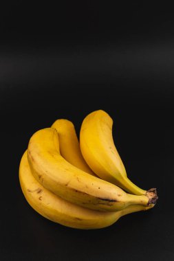 Bir grup olgun sarı muz zıt bir karanlık yüzey üzerinde bir araya gelir, canlı renklerini ve pürüzsüz dokusunu gösterir, sağlıklı atıştırma ve pişirme için mükemmeldir..