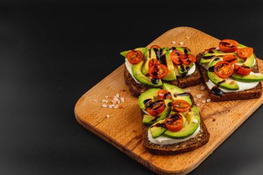 Lezzetli vejetaryen tostu kremalı avokado dilimleri, taze vişneli domatesler ve ahşap bir tahtanın üzerine serpiştirilmiş balzamik jöle. Mükemmel aperatif veya aperatif seçeneği.