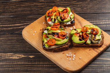 Dilimlenmiş avokado, vişneli domates ve balzamik jöleli lezzetli çavdar ekmeği. Tahta tahtada servis edilen sağlıklı bir brunch seçeneği için mükemmel..
