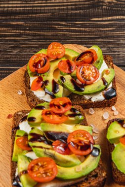 Taze avokado ve kiraz domatesleri kızarmış ekmeğin üzerine serpilmiş, balzamik sirke serpiştirilmiş ve tuz serpiştirilmiş, besleyici bir kahvaltı veya atıştırmalık için mükemmel..
