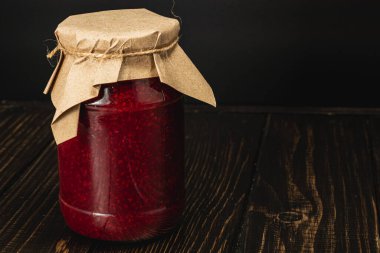 Parlak kırmızı ahududu ve kiraz reçeli, üzerinde kahverengi kağıt kapağı olan büyük bir cam kavanozu doldurur. Bu baştan çıkarıcı ev yapımı vitrinler zevk için korunmuş taze meyvelerin bir karışımı..