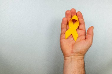 Bir insan avucunun içinde sarı bir farkındalık şeridi tutarak kanser farkındalığını ve hastalıklara karşı mücadeleyi sembolize ediyor..