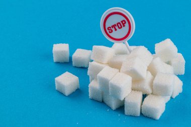 Bir küp şeker yığını, üzerinde kırmızı ve beyaz yuvarlak bir tabela bulunan parlak mavi bir arkaplanda oturur ve 