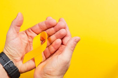 Kanserle mücadelede umut ve desteği sembolize eden ve hastalar için farkındalığı artıran parlak sarı bir kurdele tutan iki el..