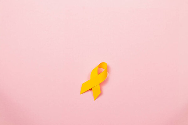 A yellow ribbon rests against a pastel pink background, symbolizing awareness and support for cancer patients. This representation emphasizes hope, courage, and the ongoing struggle against illness.