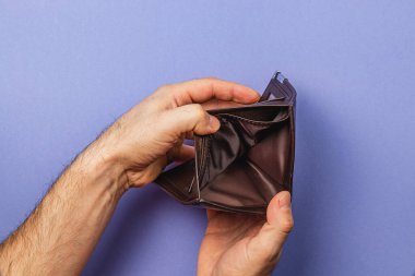 Erkek bir iş adamı boş cüzdanını inceliyor, umutsuzluk ve kayıp hislerini yansıtıyor. Bu an ekonomik zorlukların ve finansal yüklerin acı gerçekliğini gösteriyor..