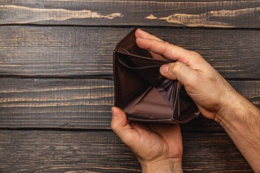 Erkek bir işadamı boş cüzdanını endişeli bir ifadeyle inceliyor. Ekonomik durgunluğun etkisini vurgulayan mali sıkıntıları ve para sorunlarını yansıtıyor..