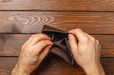 Boş cüzdanını endişeyle inceleyen bir adam, günümüz ekonomisindeki yoksulluk ve iş kaybı gibi finansal zorlukların derin etkilerini gözler önüne seriyor..
