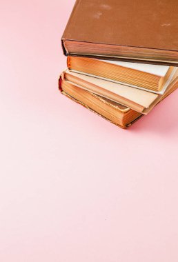 Yıpranmış kapaklarını ve altın kenarlı sayfalarını vurgulayan yumuşak pembe bir yüzeye yığılmış klasik kitap koleksiyonu. Bu kurgu sıcak, nostaljik bir okuma titreşimi yakalar..