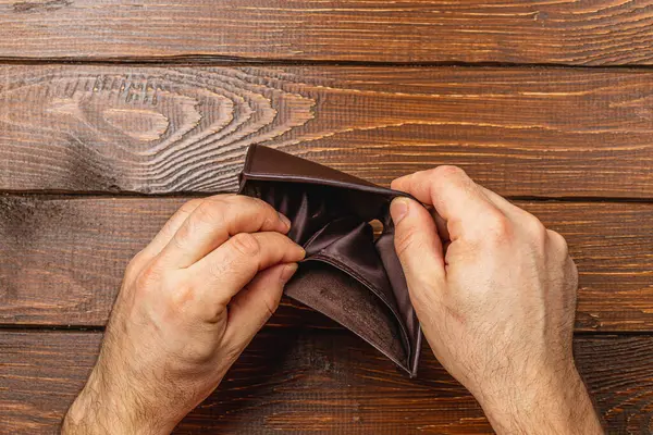 Boş cüzdanını endişeyle inceleyen bir adam, günümüz ekonomisindeki yoksulluk ve iş kaybı gibi finansal zorlukların derin etkilerini gözler önüne seriyor..
