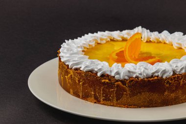 Pofuduk kremayla kaplanmış parlak turuncu dolgulu canlı bir pasta beyaz bir tabakta güzelce sergilenir. Portakal dilimleri ferahlatıcı bir dokunuş ekler.