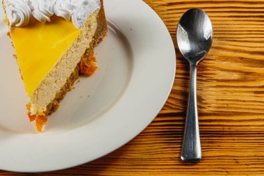 Parlak bir kaşığın yanında beyaz bir tabakta duran kremalı pastanın güzel bir dilimi sıcak, kırsal bir kafe atmosferine hoşgörü katıyor..