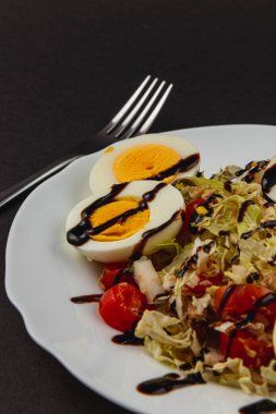 Kıtır marul, vişneli domates ve kaynamış yumurta içeren renkli salata. Bol balzamik bir jöle ile serpiştirilmiş. Koyu bir yüzeye karşı beyaz bir tabakta zarif bir şekilde sunuluyor..