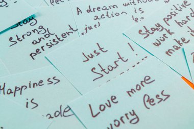 Düz bir yüzeye yerleştirilmiş el yazısı motivasyon alıntıları içeren çeşitli kağıt kartlar. Her kart, azim ve mutluluğu teşvik etmek amacıyla farklı bir pozitif mesaj iletir..