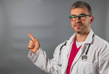 Beyaz önlüklü ve gözlüklü bir doktor, tıbbi bir ortamda önemli sağlık bilgilerini paylaşmaya hazırlanan bir sergiye dikkat çekiyor. Ayarlar profesyonelliği yansıtıyor.