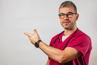 Önlük giymiş bir sağlık çalışanı kendinden emin bir şekilde bir tarafı işaret ediyor ve misafirperver bir tavır sergiliyor. Ortam parlak ve tarafsız, profesyonel bir ortam için ideal..