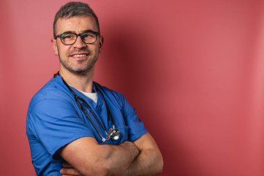 Bir sağlık uzmanı kollarını kavuşturup, kendine güvenini göstererek gülümsüyor. Arka plan sıcak bir tondur, o anın profesyonel atmosferini arttırır..