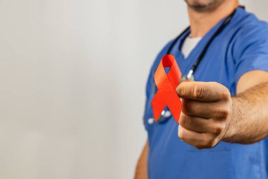 Önlerinde canlı kırmızı bir kurdele tutan bir sağlık çalışanı, sağlık sorunları için farkındalık ve desteği sembolize ediyor. İşçi önlük giymiş ve boyunlarında steteskop var..