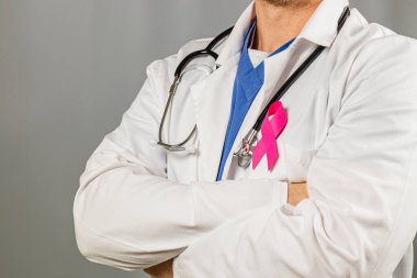 Kollarını kavuşturmuş, laboratuvar önlüğündeki pembe kurdeleyi gösteren bir sağlık uzmanı göğüs kanseri farkındalığını sembolize ediyor. Ayarlama bir dayanışma mesajı iletiyor.