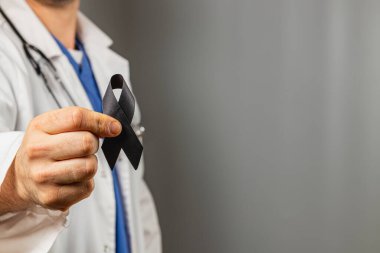 Beyaz önlük ve steteskop giyen bir sağlık uzmanı siyah bir kurdele taşır, bu da anma ya da desteği simgeler. Tarafsız bir ortam, dayanışma mesajını vurguluyor..