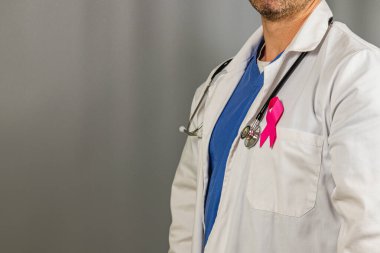 Bir sağlık uzmanı, beyaz önlük ve önlükle, meme kanseri farkındalığı için pembe bir kurdele göstererek, sağlık savunuculuğuna olan bağlılığını vurgulayarak,.