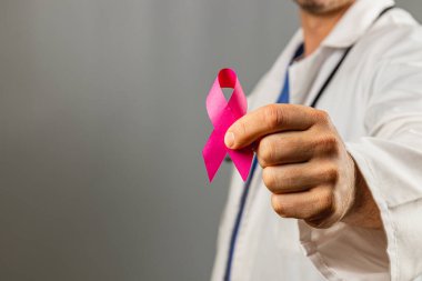 Beyaz önlüklü bir doktor meme kanseri farkındalığını arttırmak için pembe kurdele tutuyor. Ayar, Ekim ayında sağlık eğitimi ve toplum desteğinin önemini vurguluyor..