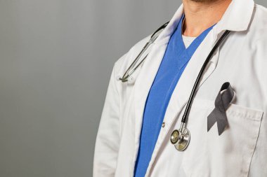 Bir sağlık görevlisi beyaz önlük ve boynunda steteskop olan mavi önlük giyiyor. Siyah kurdele önemli bir amaç için destek ve farkındalığın sembolü olarak sergilenir..