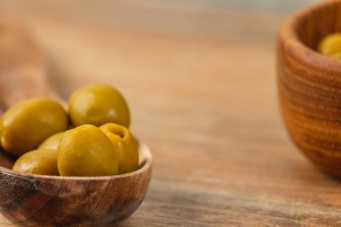 Yeşil zeytinler küçük ahşap kaselerde dikkatlice düzenlenir, kırsal ahşap bir yüzeye yerleştirilir. Tahtanın doğal dokusu zeytinlerin canlı rengini tamamlar ve sağlıklı bir ortam yaratır..