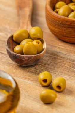 Taze yeşil zeytinler ahşap bir kaşığa, kaselerin yanına konur. Ayarlama yemek pişirmek ya da aperatif hazırlamak için mükemmel bir mutfak temasını vurgular.