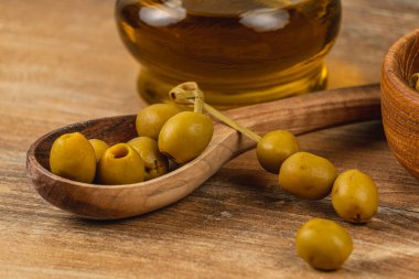 Tahta bir kaşık taze yeşil zeytin tutar, yanında da küçük bir kase zeytinyağı. Bu iştah açıcı düzenleme malzemelerin doğal dokularını ve renklerini vurgular..