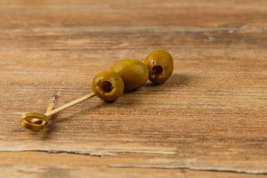 Kürdandaki üç yeşil zeytin, ahşap bir yüzeyde dinleniyor. Sıradan bir yemek deneyimi için mükemmel. Toplantılarda atıştırmak için ideal. Lezzetli bir tat sunuyorlar..