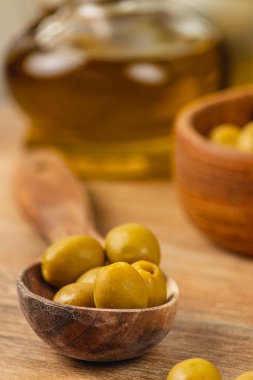 Yeşil zeytinler arka planda görünen zeytinyağı yağmuru ile küçük bir ahşap kasede düzenlenir ve kırsal bir mutfakta davetkar bir mutfak atmosferi yaratır..