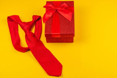 Parlak sarı arka plan, canlı kırmızı kurdeleye sarılı bir hediye kutusunun yanına yerleştirilmiş kırmızı bir kravatı ön plana çıkarıyor. Babalar Günü 'nü ya da doğum gününü kutlamak için ideal. Bu düzenek, düşünceli bir hediyeyi temsil ediyor..