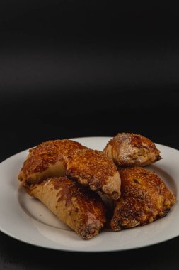 Bir tabakta cazip bir yığın balkabağı pastası sergilenir, altın kahverengisi ve hafif şekerle tozlanmış. Koyu arkaplan, taze pişmiş dokularını ve davetkar görünüşlerini ön plana çıkarıyor..