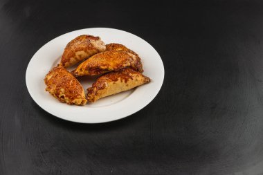 Sıcak ve altın balkabağı dolgulu börekler siyah bir zemine karşı beyaz bir tabakta otururlar. Hamur işlerinin çıtır çıtır bir yüzeyi var, herkesi bir ısırık almaya ve tatlılığının tadını çıkarmaya davet ediyor..