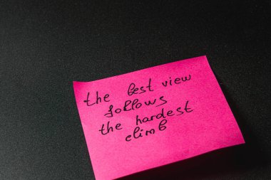 Pembe yapışkan bir notta zorlukların üstesinden gelmek hakkında ilham verici bir mesaj yer alıyor. El yazısıyla yazılan kelimeler azmin ödüllendirici deneyimlere yol açtığını vurgular. Bu olumlu bir zihniyeti teşvik eder..