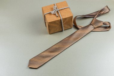 Güzelce hazırlanmış bir kravat, düzgün paketlenmiş bir hediye kutusunun yanında duruyor. Babalar günü ya da doğum günü kutlaması için ideal bir hediye sunuyor. Bu anlaşma onurlu babaların özünü yansıtıyor..