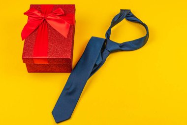 Babalar Günü 'nün canlı bir kutlaması, klasik bir mavi kravatın yanına takılmış kırmızı bir hediye kutusunu içeriyor. Bu düzenleme, özel bir durum için düşünceli bir hediyeyi temsil eder..