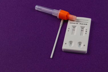 Bir COVID-19 ve grip test kiti mor bir yüzeye oturmuş, uygulamalı bir koleksiyon tüpü ve etkili sağlık izleme için kolay okunabilen bir sonuç paneli içeriyor.