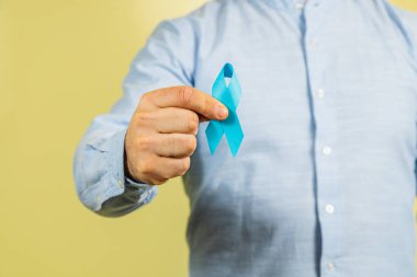 Adamın biri prostat kanseri farkındalığını sembolize eden mavi bir kurdele tutuyor. Bu kampanya, hastalıktan etkilenenler için sağlık bilincinin ve desteğin önemini vurguluyor..