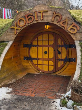 Yaremche Ukrayna 21.01.25 Hobbit deliği gibi tasarlanmış çekici bir bar girişi demir aksanlı yuvarlak ahşap bir kapıya sahiptir. Etrafı yeşilliklerle çevrili olan bina, ziyaretçileri tuhaf bir yemek deneyimine davet ediyor..