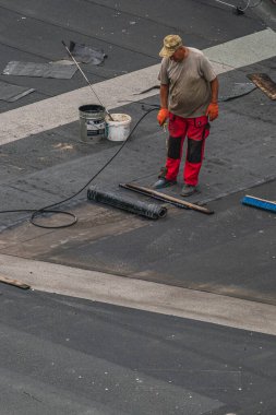 Kırmızı pantolonlu ve turuncu gömlekli bir inşaat işçisi, 27 Ağustos 2024 'te Ukrayna' nın Lviv kentindeki bir binanın çatı onarımında görev aldı. Cihazlar ve rulo malzemeler yakında..