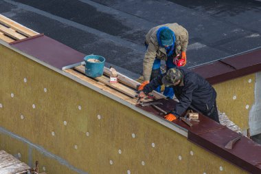 Lviv, Ukrayna 16 Ekim 2024 iki inşaat işçisi çatıda tamirat yapmakla meşgul. Bina üzerinde çalışırken çeşitli araç ve gereç kullanıyorlar..