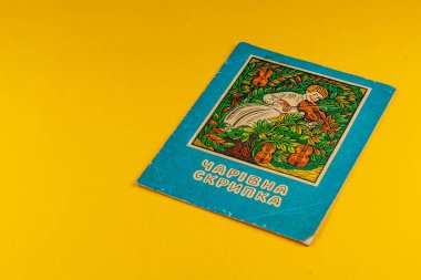 25.03.25 Lviv Ukrayna. Charivna Skrypka başlıklı klasik bir Ukrayna kitabı. Yeşillik ve canlı çiçekler arasında keman çalan bir kızın resimli bir kapağı..